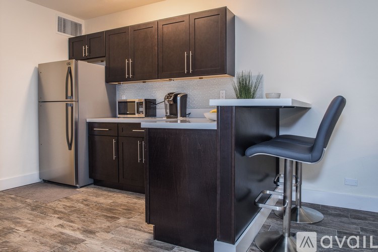 A kitchen with a refrigerator, microwave, and bar stool.