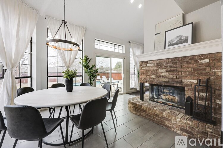 A modern dining room with a round table and chairs, a fireplace, and a large window.