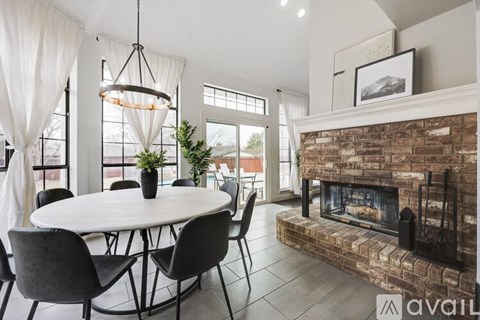 A modern dining room with a round table and chairs, a fireplace, and a large window.