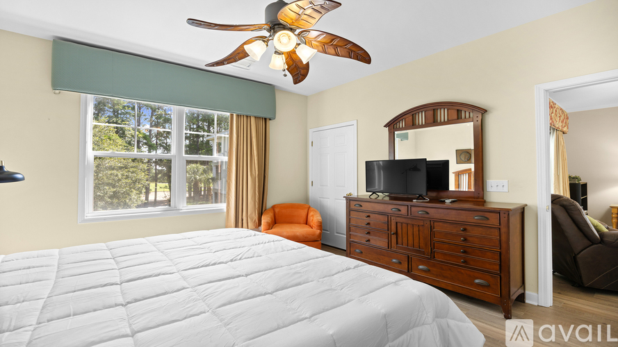 A bedroom with a large bed, a ceiling fan, and a dresser with a mirror.