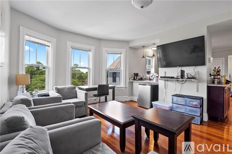 A living room with a grey couch, a wooden table, and a television mounted on the wall.