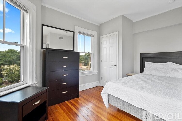 A bedroom with a large bed, a dresser, and a window overlooking a tree-filled landscape.