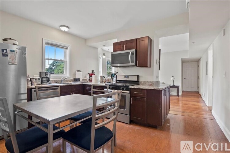 A kitchen with a table and chairs in the foreground and a refrigerator, microwave, oven, and sink in the background.