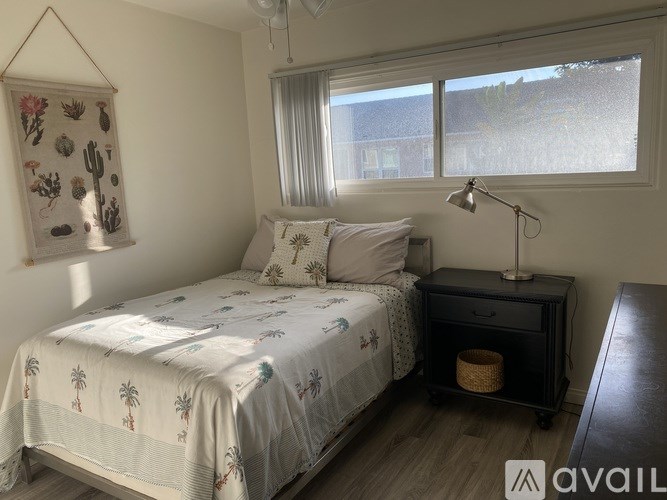 A bedroom with a bed, nightstand, and a wall hanging with cacti.