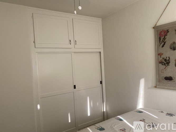 A white bedroom with a bed, wardrobe and a hanging picture.