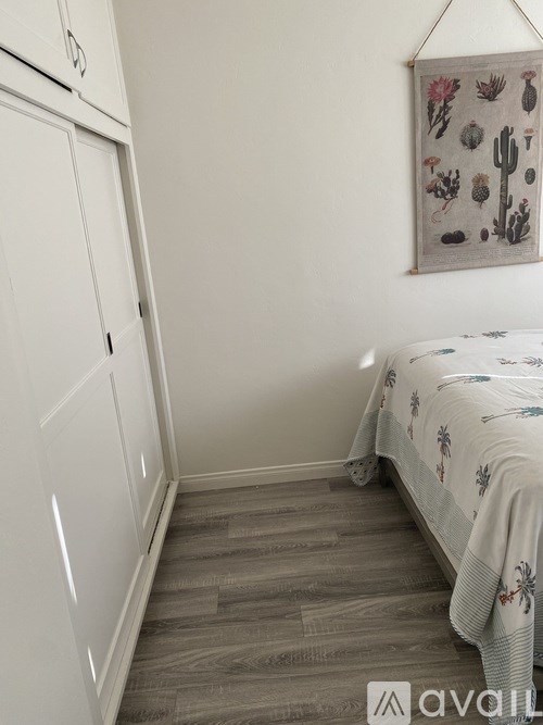 A bedroom with a bed, a wardrobe, and a wall hanging with cacti.