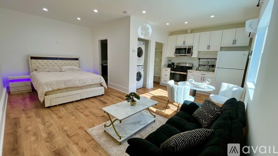 A modern bedroom with a large bed and a kitchen area in the background.