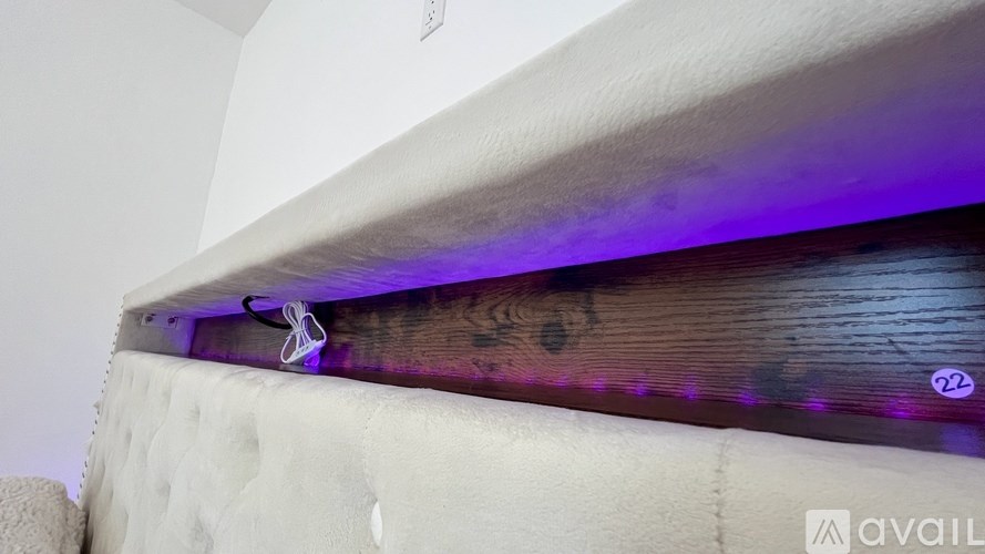 A bed with a white mattress and a purple light underneath it.