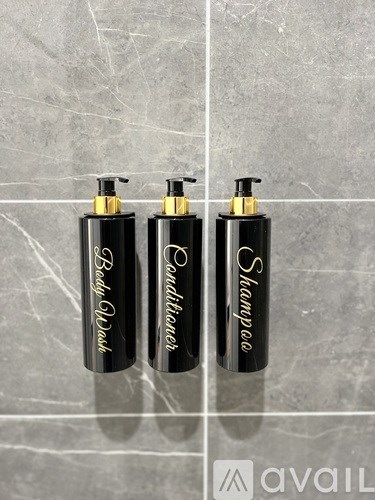 Three black bottles of shampoo and body wash on a marble surface.