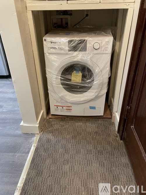 A washing machine is wrapped in plastic and sitting in a doorway.