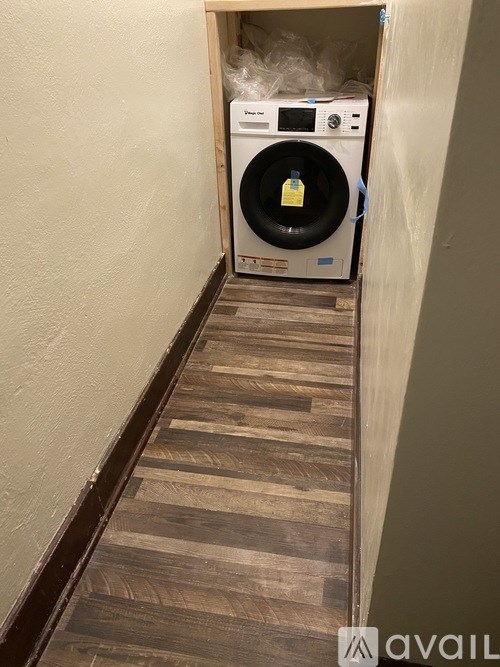 A washing machine is in a narrow hallway with wooden floors.