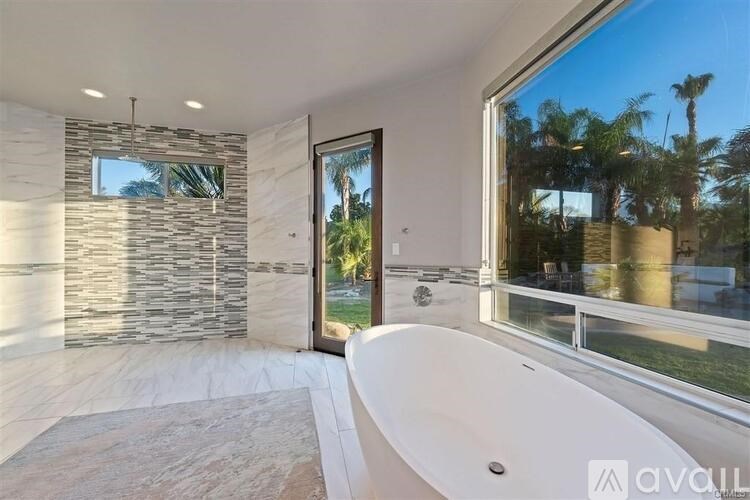 A modern bathroom with a large tub and a view of palm trees outside.