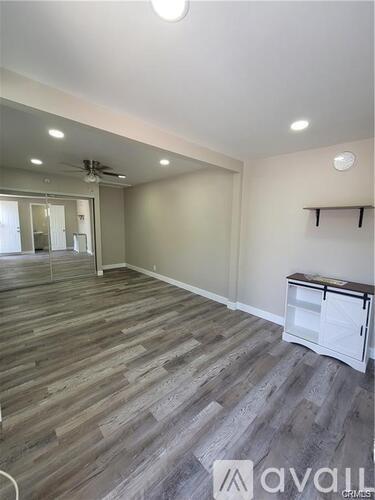 A room with a ceiling fan and grey wood flooring.