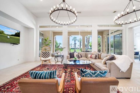 A living room with a large rug and a TV on the wall.