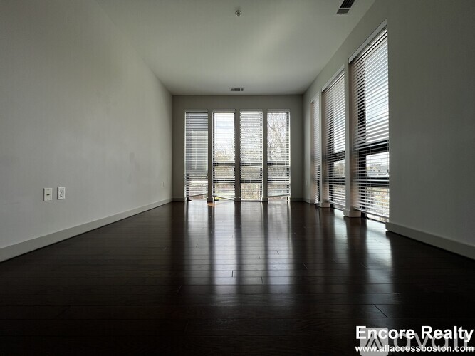 A spacious room with wooden floors and large windows.