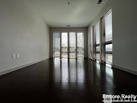 A spacious room with wooden floors and large windows.