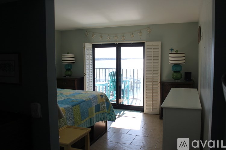 A bedroom with a bed, a nightstand, and a balcony with a view of the ocean.