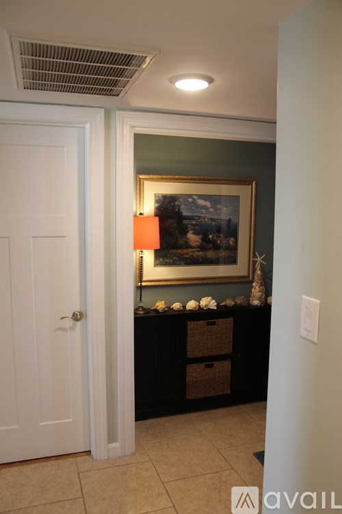 A painting hangs on a wall above a black table with a white vase on it.