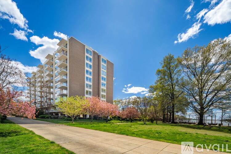 A tall apartment building with a walkway in front of it and trees with pink blossoms in the foreground.