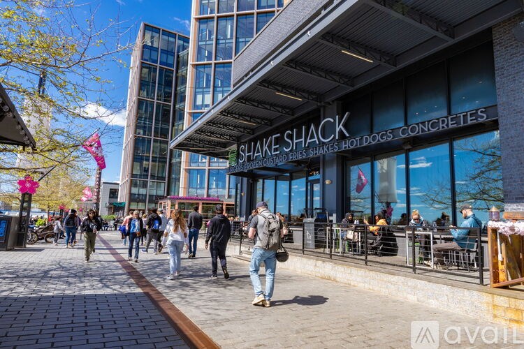 A group of people are walking on a sidewalk in front of a Shake Shack restaurant.