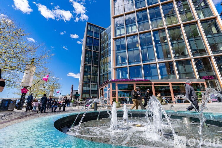 A fountain in front of a modern building with people walking around.