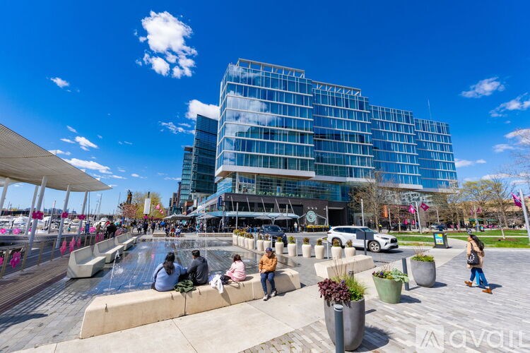 People are sitting and walking around a skate park in front of a modern glass building.