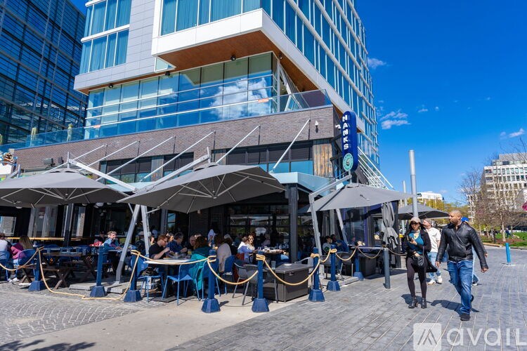 A group of people are walking past a restaurant with blue tables and chairs.