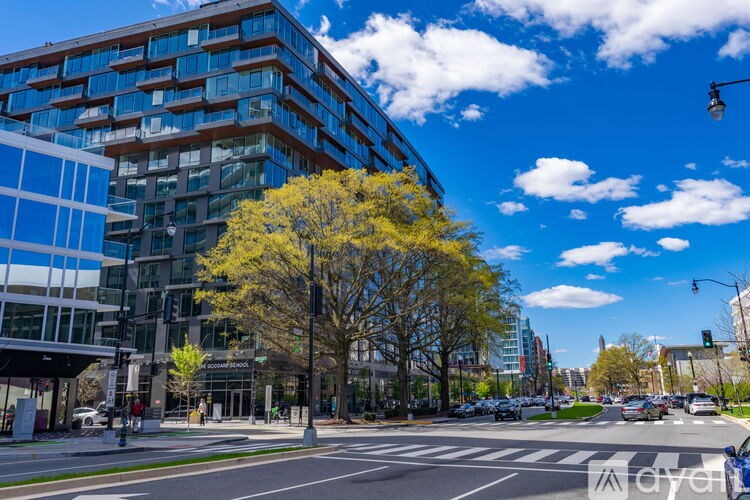 A modern building with a glass facade is surrounded by trees and a clear blue sky.