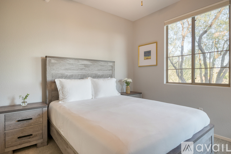 A bedroom with a large bed, a nightstand with a plant, and a framed picture on the wall.