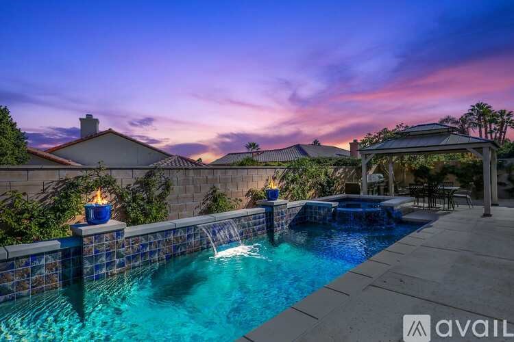 A pool with a waterfall and a patio area with a table and chairs.