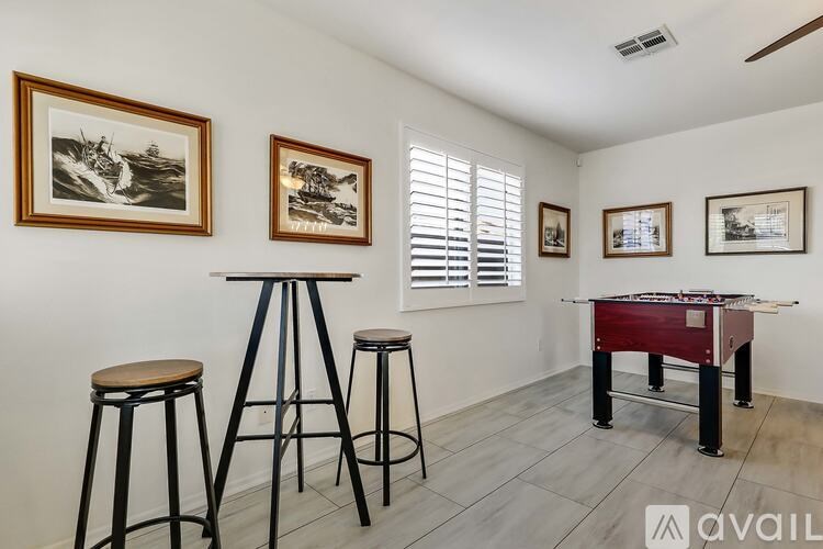 A room with a pool table, two stools, and pictures on the wall.