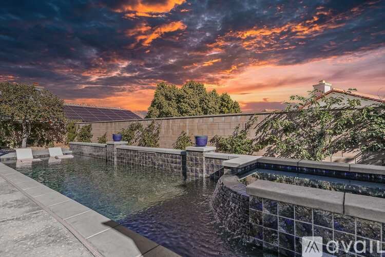 A pool with a waterfall surrounded by trees and a sunset in the background.