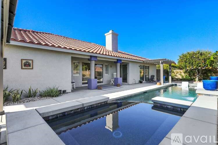 A white house with a red tile roof and a pool in front.