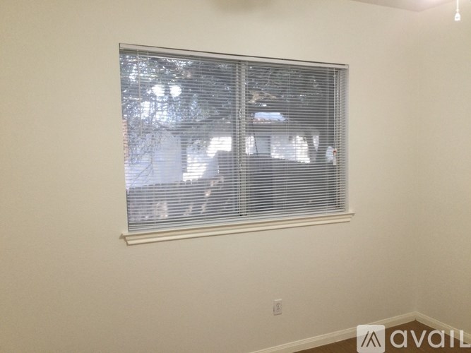 A window with blinds in a room with a view of a house.