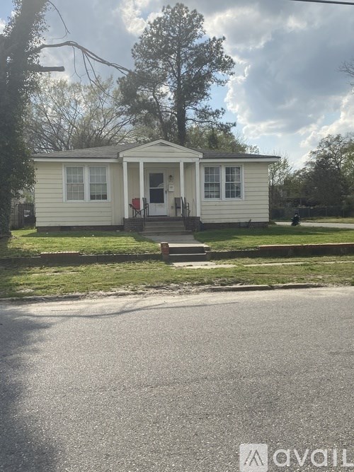 A small white house with a front porch and a tree in front.