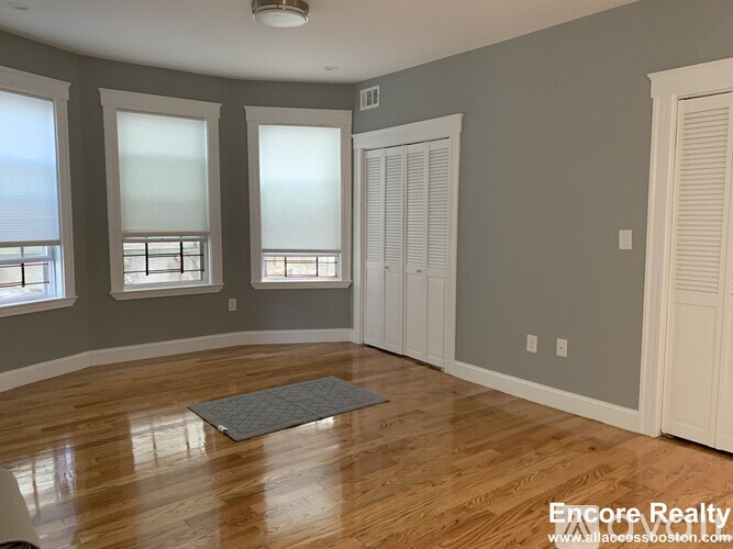 A room with wooden floors and a grey rug in the middle.