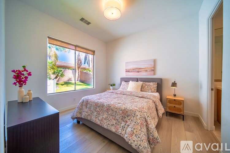 A bedroom with a bed, nightstand, and a window with a view of a house and trees.