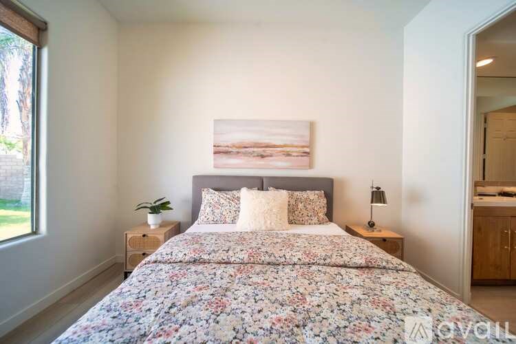 A bedroom with a floral bedspread and a painting on the wall.