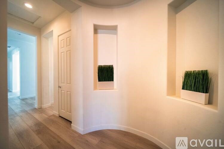 A hallway with a wooden floor and white walls, with two framed green plants on the wall.