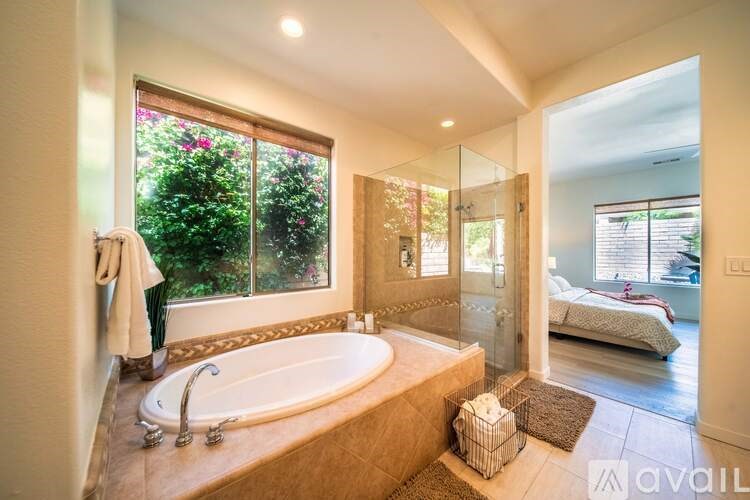 A bathroom with a large tub and a view of a bedroom through a glass door.