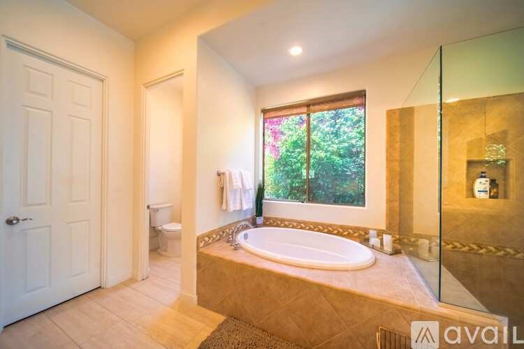 A bathroom with a large tub and a window overlooking a green landscape.