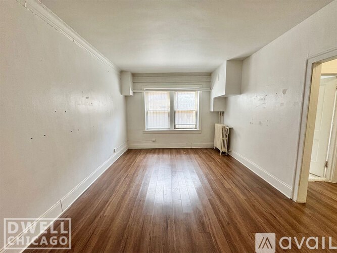 A room with wooden floors and white walls, with a window and a door visible.
