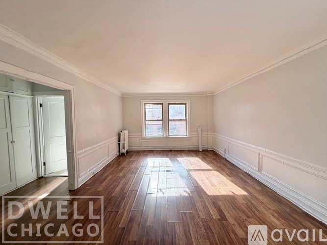 A room with wooden flooring and white walls, with a doorway leading to another room.