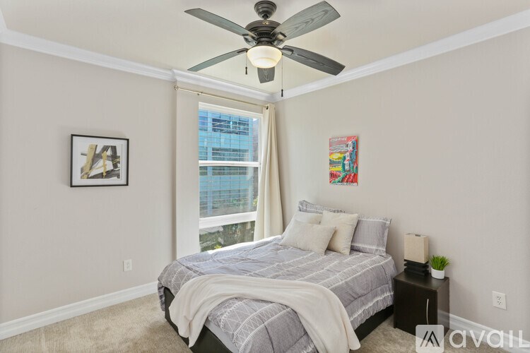 A bedroom with a bed, a ceiling fan, and a window with a view of a building outside.