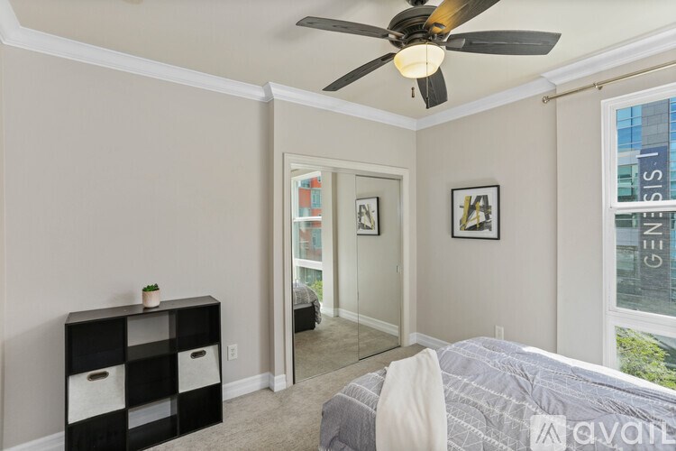 A bedroom with a bed, a ceiling fan, and a window with a view of a city.