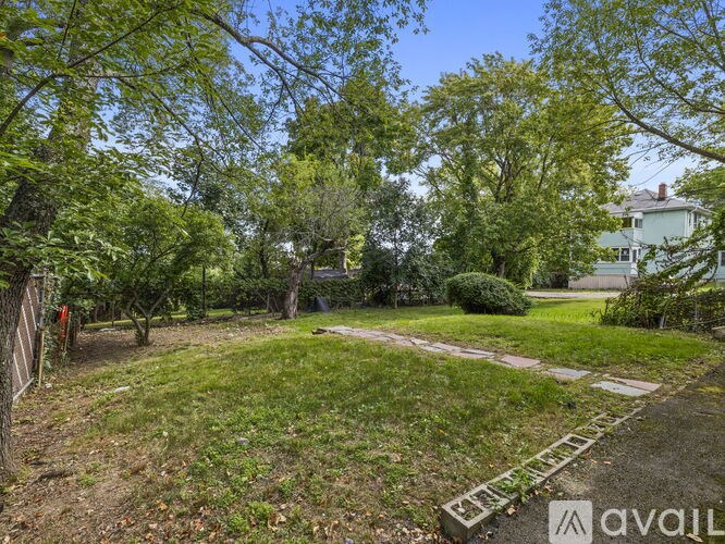 A backyard with a lawn, trees, and a white house in the background.