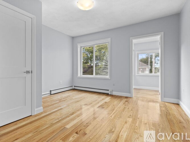 A room with wooden flooring and two windows.