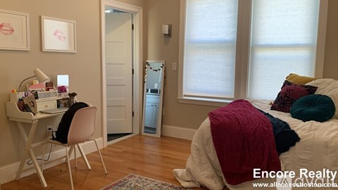 A bedroom with a bed, desk, chair, and a window.