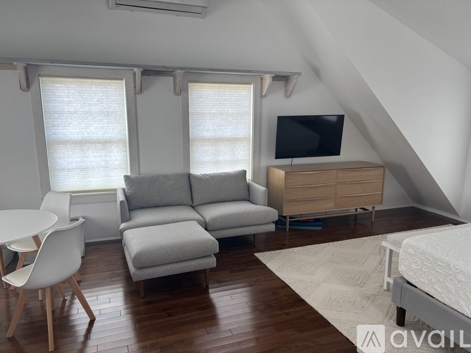 A living room with a grey couch, a white chair, a wooden floor, and a television on a cabinet.