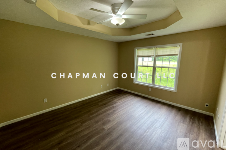 A room with a ceiling fan and a window showing a view of a grassy area.